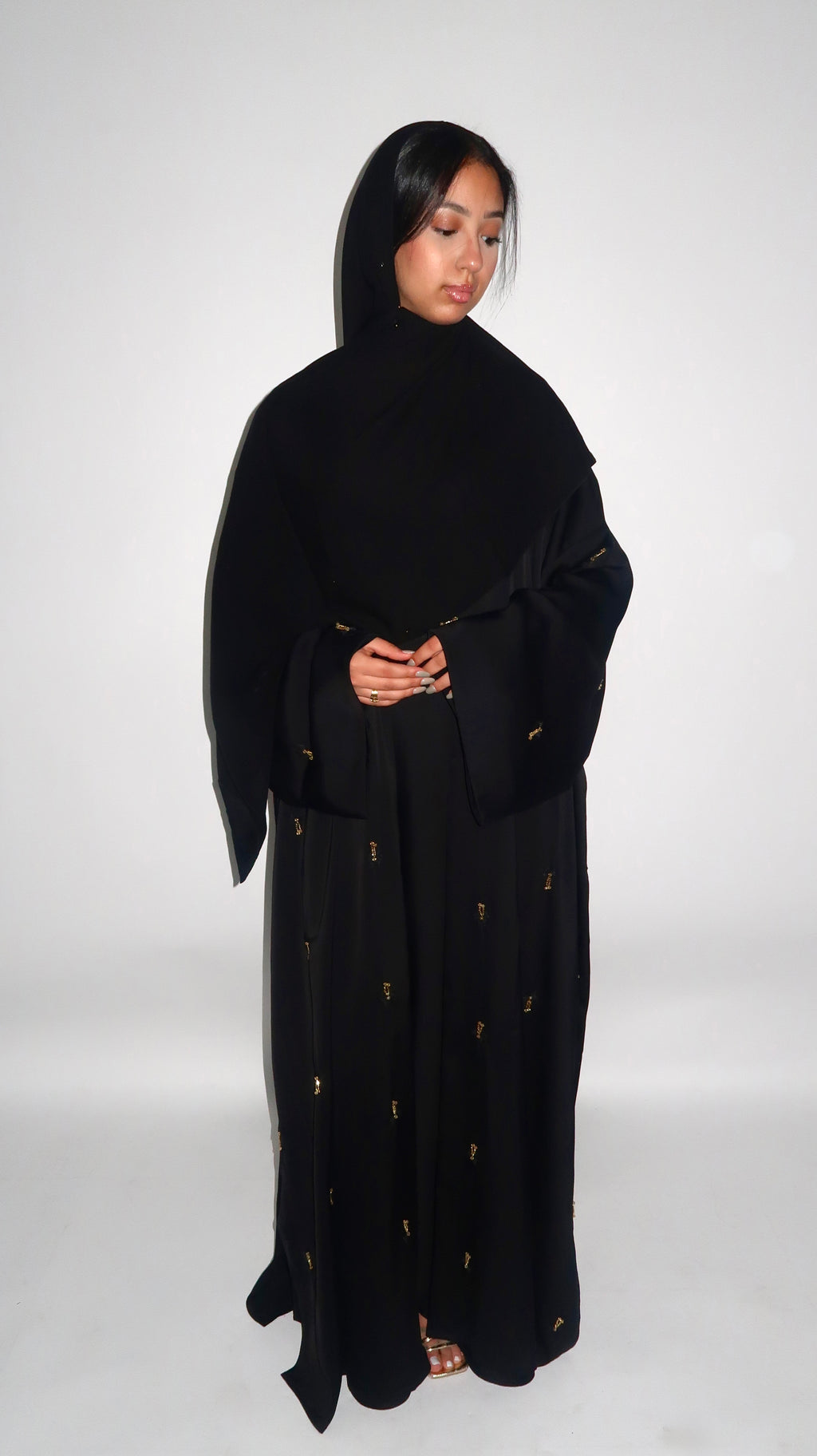 Woman wearing a black abaya with gold details on a white background